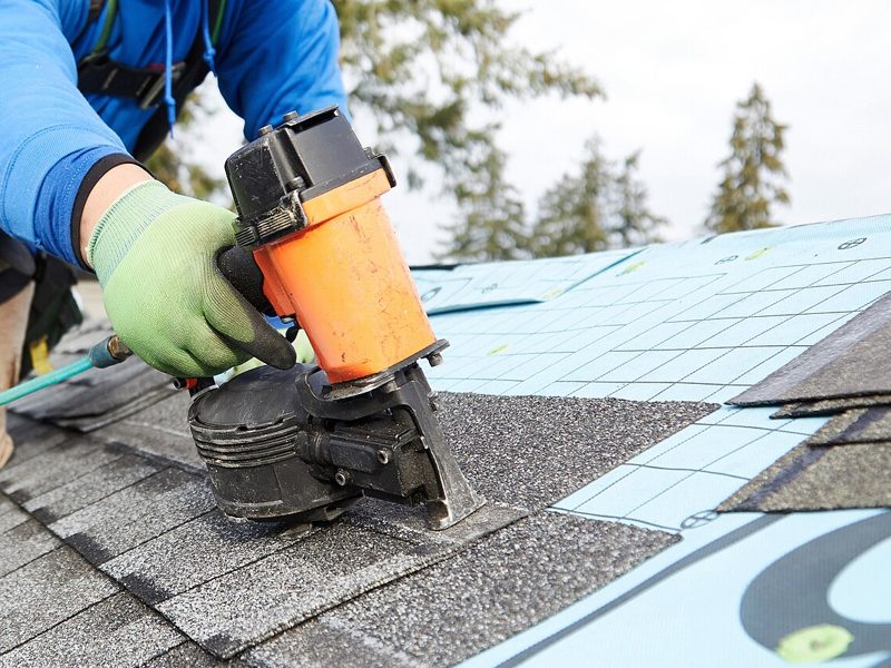 A roofer harnessed on a pitched roof, fixing shingles