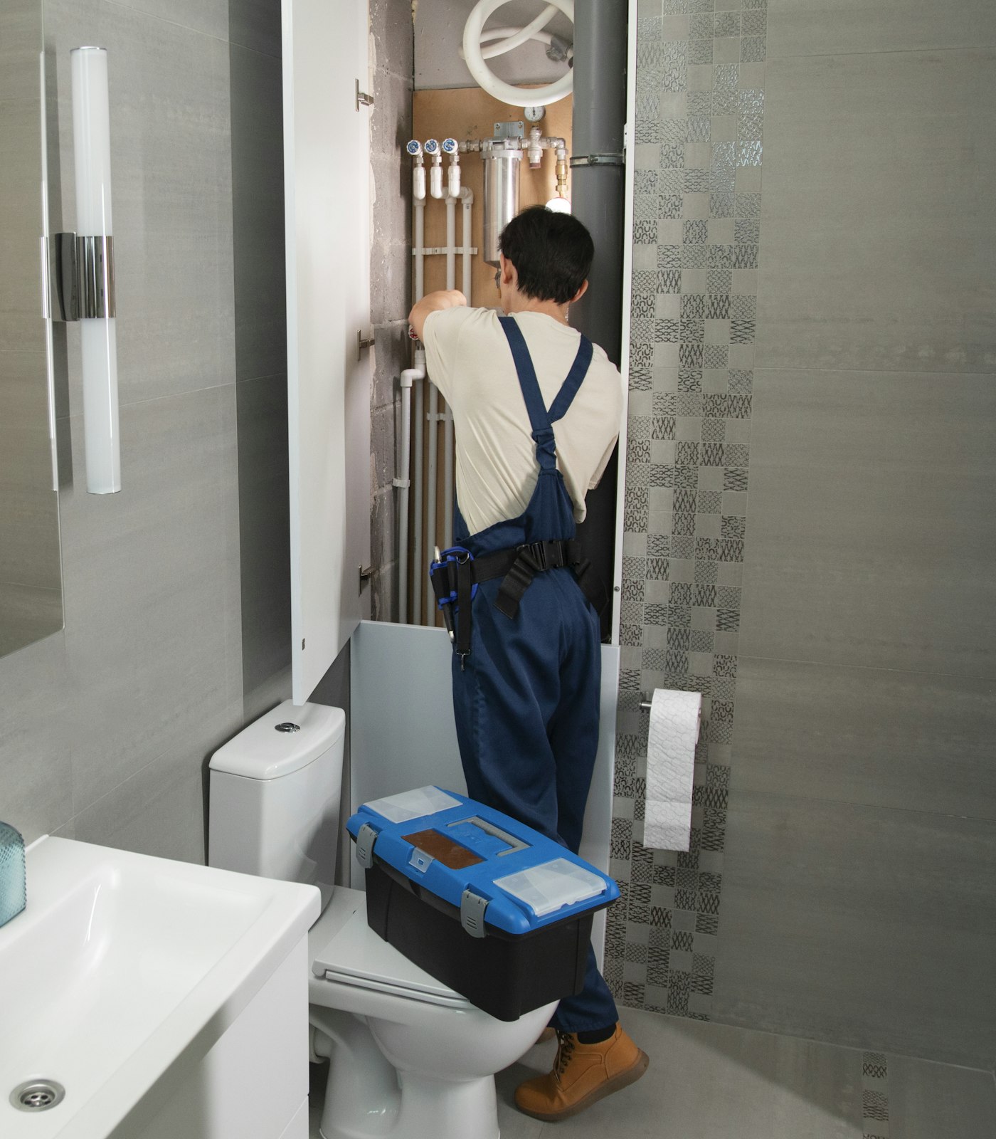 A plumber tightening a valve under a sink with a wrench